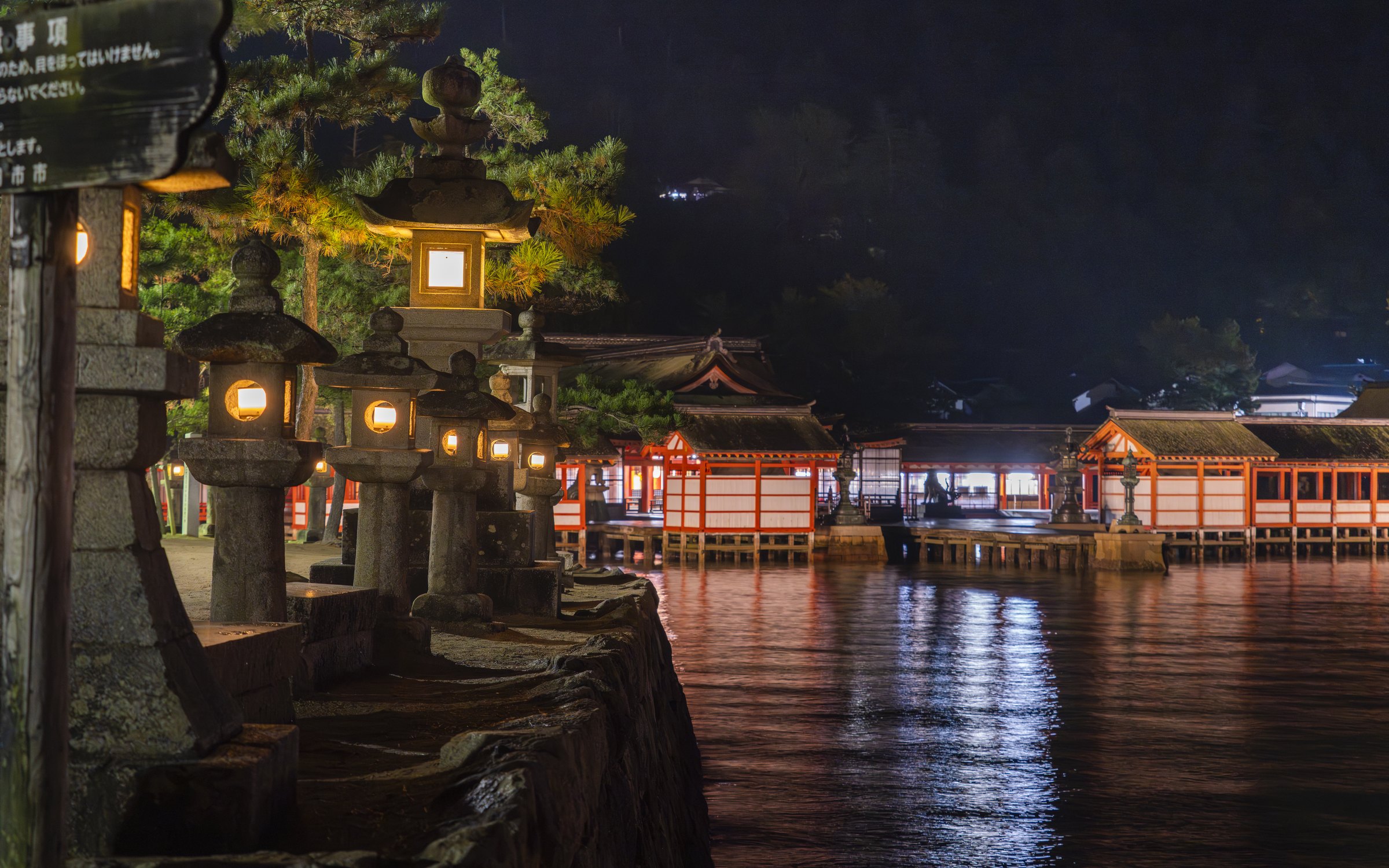 The great torii gate of Itsukushima Shrine lit at night, mirrored on the water
