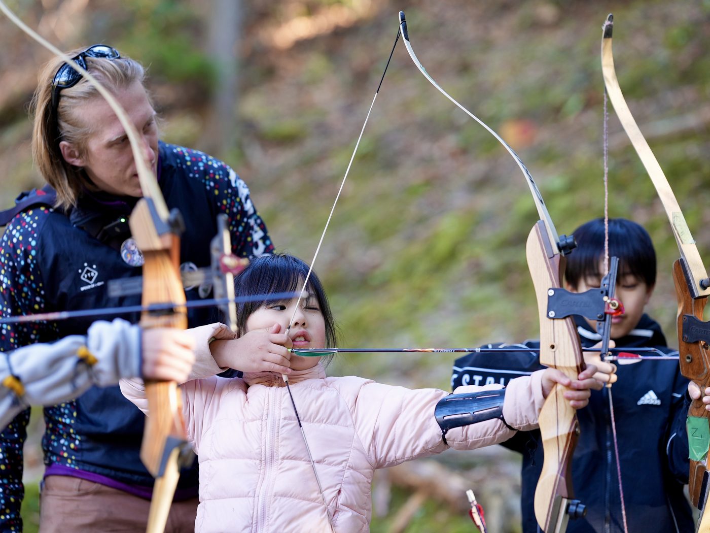 A guide steadying a child's hand as she draws a bow