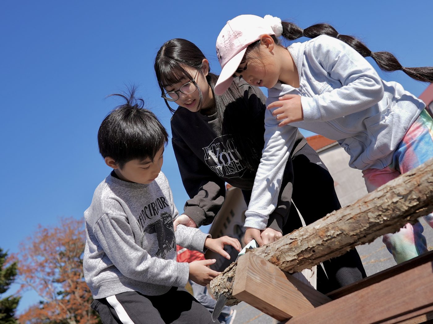 Children sawing a log under a deep blue sky